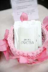 Delicate tissue packets, designed for happy tears, sit elegantly in a pink woven basket with decorative pink petals, offering a heartfelt touch for wedding ceremonies or celebrations.