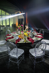 Elegant round dinner table set with white chairs, vibrant flowers, and neatly arranged napkins in an event space featuring a large heart-shaped display as a backdrop.