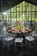  Elegant round dinner table set with white chairs, vibrant flowers, and neatly arranged napkins in an event space featuring a large heart-shaped display as a backdrop.