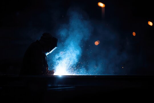 capture minimalistic scene of welder working on metal structures while sparks fly against darkened backdrop to emphasize