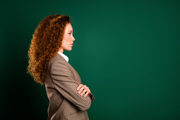 Confident businesswoman with red curly hair in formal suit against emerald green background...