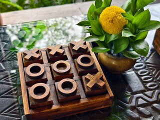 A handcrafted wooden tic-tac-toe board and a brass flower vase