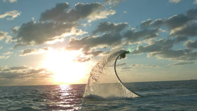 Silhouette of person on water hoverboard flipping over ocean with distant sunset - super slow motion at 1000 FPS