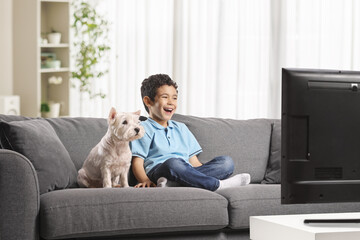 Kid and dog sitting on a sofa at home watching tv