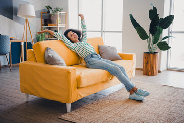 Young woman relaxing on a vibrant yellow sofa in a stylish living room filled with natural light...