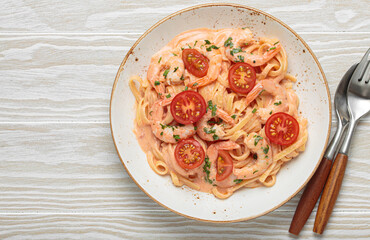 Seafood linguine pasta in creamy sauce with shrimp and cherry tomatoes, garnished with fresh parsley, served on white wooden background with cutlery top view, copy space