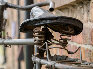 Close-up of a old sprung vintage bicycle saddle against a brick wall.