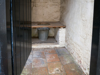 Rustic outdoor latrine toilet with wooden bench and metal bucket.