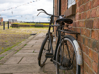 Old vintage bicycle leaning against a brick wall on a quiet cobblestone street.