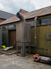 Industrial exhaust system beside a weathered building on a cloudy day.