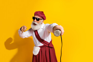 Cheerful elderly man wearing traditional Scottish attire with microphone on vibrant yellow...