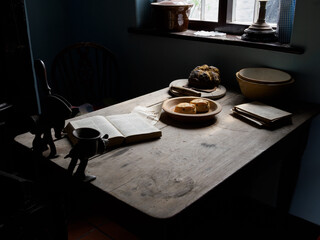 Cozy kitchen table with bread and cheese with open book in dim window lighting.
