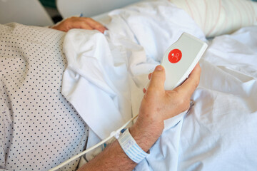 Hospitalized patient wearing dotted pajamas holding nurse call button in hand, requesting medical assistance