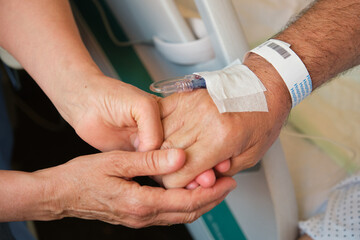 Nurse comforting elderly patient by holding his hand, providing support and empathy during hospital...