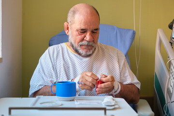 Senior man recovering in hospital bed opening cookies packet while having breakfast