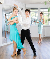 Passionate young ballroom enthusiasts, teenage girl and boy practicing graceful waltz routine in...