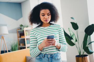 Young woman using smartphone in cozy living room with modern decor, striped shirt, and natural...