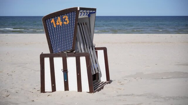 Empty hooded beach chair numbered 143 stands on a sandy beach facing the tranquil sea under a clear blue sky perfect for vacations and summer getaways for relaxing moments