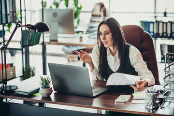 Professional businesswoman in stylish attire working at her desk in an office environment, managing documents and laptop.