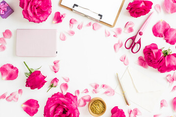 Creative workspace flat lay with roses, petals, notebook, scissors, and envelope on white background.