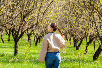 Picture in the almond orchard while a very beautiful and attractive girl walks in the bosom of nature and admires the beauty of our planet. She is happy and this walk is a relaxation for her.