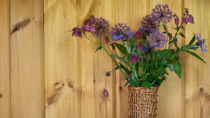 Fresh wildflowers in woven basket against wooden wall background  