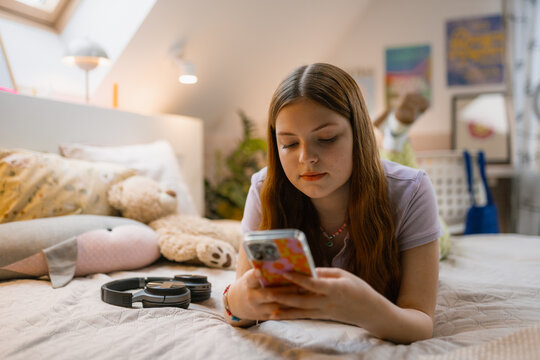 A young woman uses a mobile phone lying on the bed. Youth Bedroom
