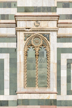Gothic bifora window with twisted columns and lion relief on the marble facade of Florence Cathedral, Italy, built in polychrome stone.