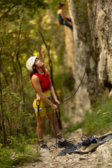 A woman in a red top and yellow shorts is looking up at a rock wall