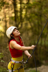A woman in a red top and yellow pants is climbing a rope