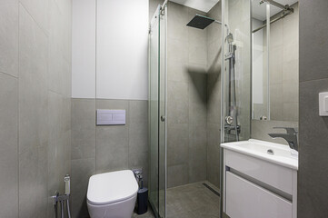Modern bathroom with gray tiles, white toilet, shower cabin with glass door, and white vanity