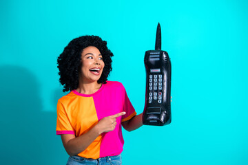 Smiling woman holding oversized retro mobile phone against a vibrant turquoise background,...