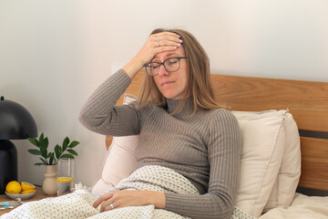 Sick caucasian female adult with headache relaxing in bed with medicine and tea nearby