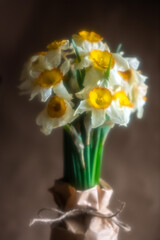 Beautiful bouquet of fresh daffodils wrapped in brown craft paper, tied with twine, creating a rustic and charming presentation on a table with soft, warm effect