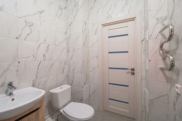modern bathroom with marble tile walls, a toilet, a sink with a wooden cabinet, a door with blue...