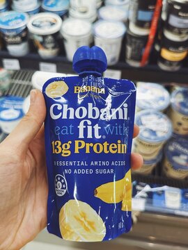 Banana-flavored Chobani yogurt pouch held in hand over a fridge shelf. Clearly labeled with protein content and health rating. Kids snack and protein on the go. Malaysia, Kuala Lumpur- May, 2025