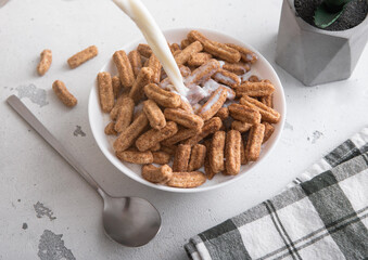 Sweet churros breakfast cereal in plate and pouring milk into it with spoon on table.Top view.