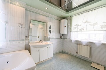 well-lit bathroom with pastel colors, featuring a tub, vanity, mirror, and water heater. Tiled walls and floors create a clean aesthetic