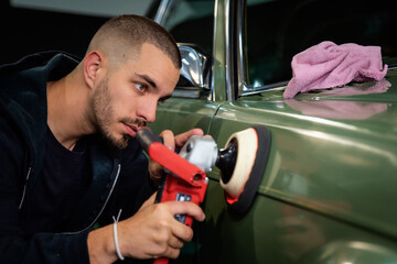 Young man using professional buffer tool to polish car