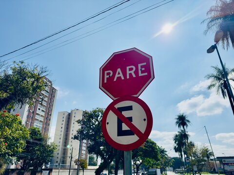 Placa de sinaliza&ccedil;&atilde;o com proibido estacionar e pare com fundo de predios urbanos.