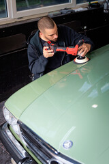 Young man using professional buffer tool to polish car