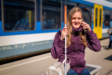 Portrait of blind woman with white cane sitting on train station outdoors in city