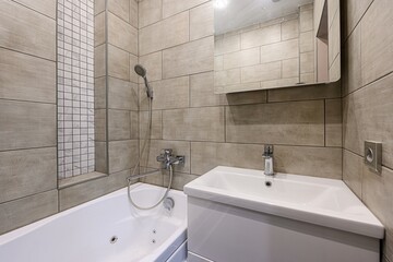 Modern bathroom featuring beige tile, white bathtub, sink, and a mirrored medicine cabinet.