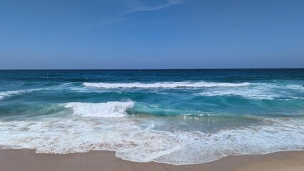 Azure Ocean Waves Crashing on Sandy Shoreline Under Clear Blue Sky, Tropical Paradise Scene