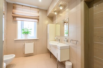 tidy, beige-tiled bathroom features a white sink vanity, a mirror, a window with a plant, and a toilet. The overall aesthetic is clean and well-lit
