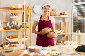 Adult woman baker in uniform holding fresh homemade bread in bakery