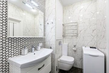 Modern bathroom featuring white marble-effect tiles, black and white mosaic accent, white sink, toilet, and washing machine