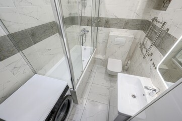 compact, modern bathroom featuring marble-patterned tiles, a glass-enclosed shower, a toilet, a...