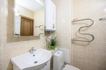 Cozy bathroom with beige tiles, white sink and toilet, a water heater, and a decorative plant.