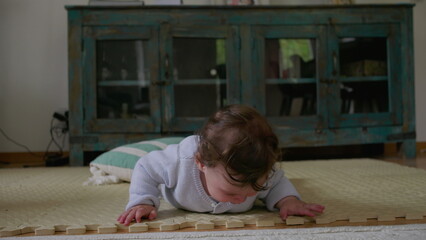 Baby lying on mat, touching and exploring textured objects with hands, focused on tactile...
